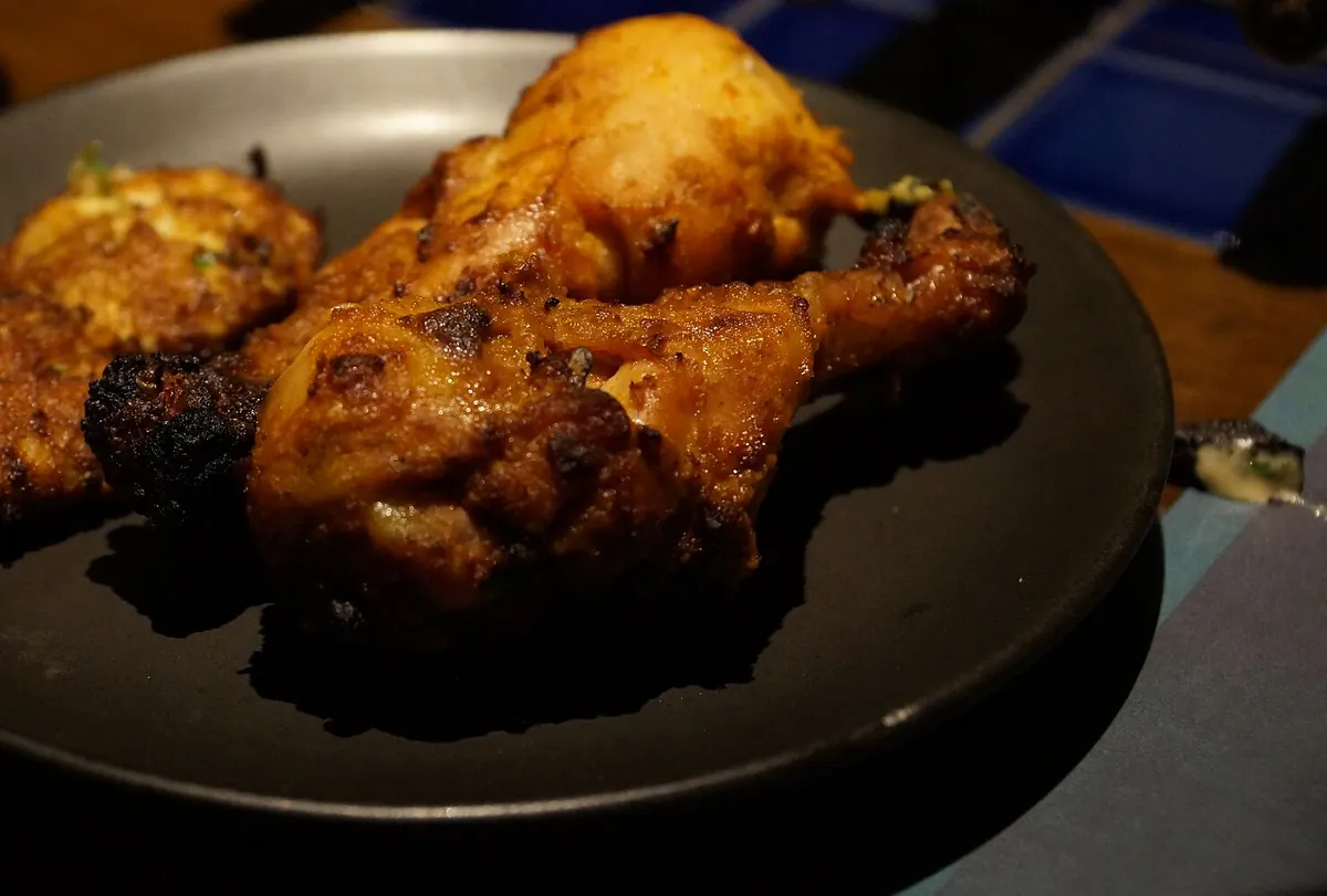 Two tandoori chicken drumsticks and a piece of chicken tikka on a dark plate